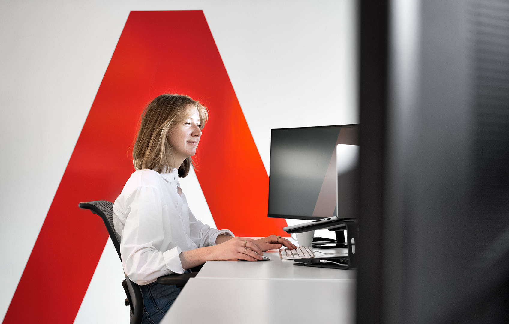 Aurélie aan het werk aan een bureau met het oranje embleem van Branderij "A" op de muur achter zich
