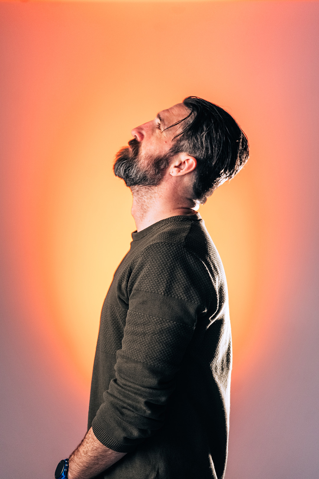 Portret van een man met baard en bril die omhoog kijkt, gefotografeerd met koel blauw licht voor een serene en introspectieve sfeer.