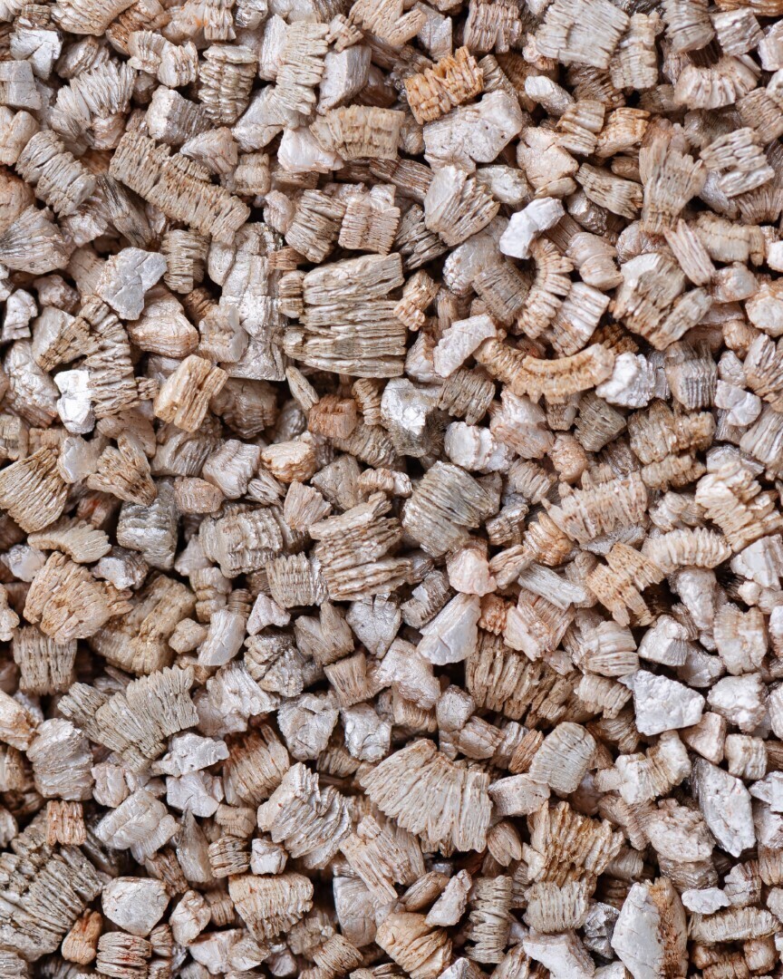 Gedetailleerde close-up van vermiculiet: een lichtbruin, glinsterend mineraal in korrelvorm, gebruikt voor isolatie of in de tuinbouw