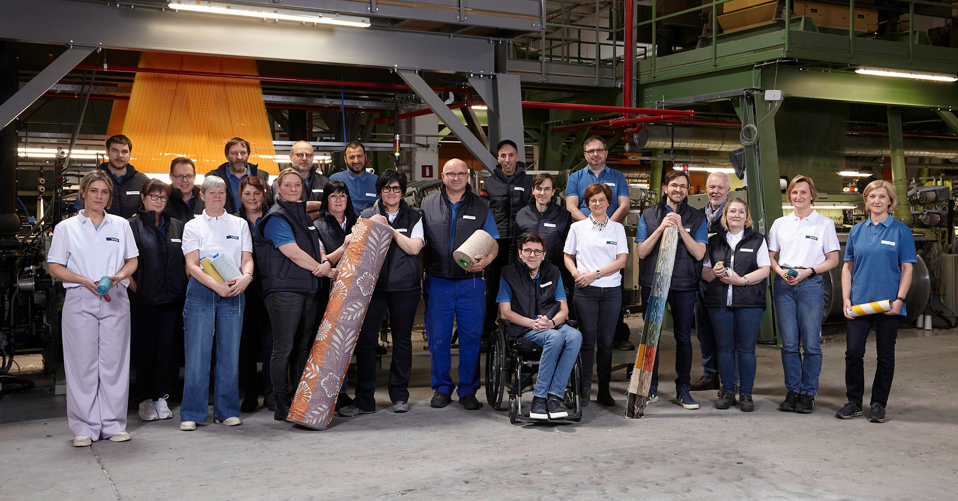 Een groepsfoto van een bedrijf waar 2 personen een rol stof vasthouden