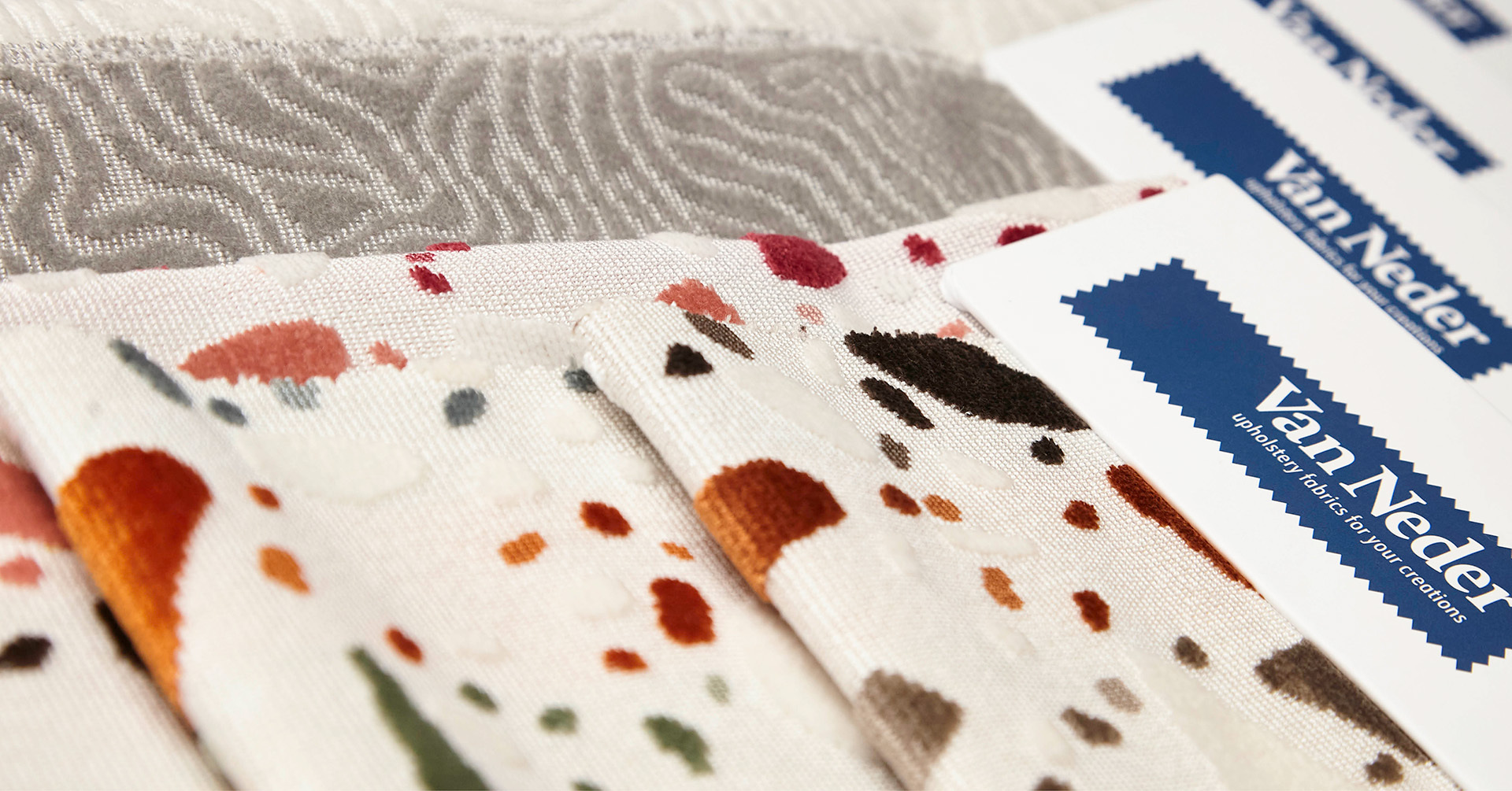 Verchillende soorten stof op elkaar gevouwd met daarboven een envelop met het logo van "Van Neder"